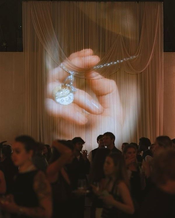 A gathering beneath a large projected image of a jewellery detail.